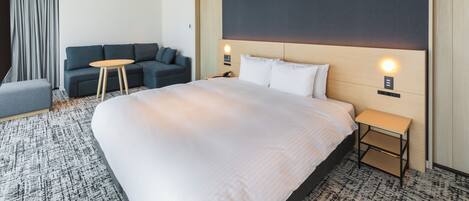 A modern hotel room with a large bed, a sofa, a small table, and a nightstand.