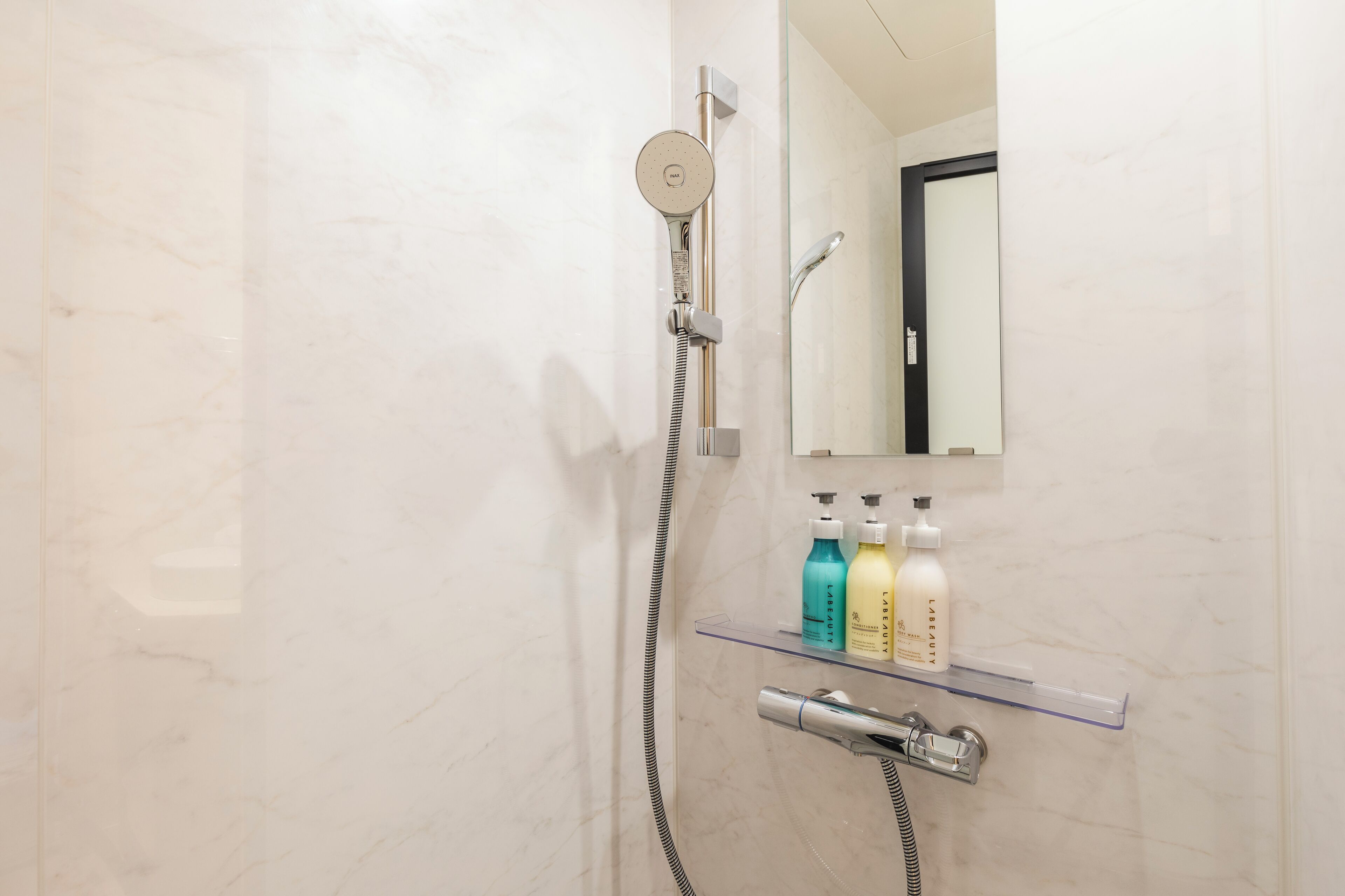 A bathroom with a shower, a mirror, and a shelf with toiletries.