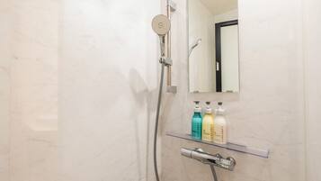 Un baño con ducha, espejo y repisa con artículos de aseo.