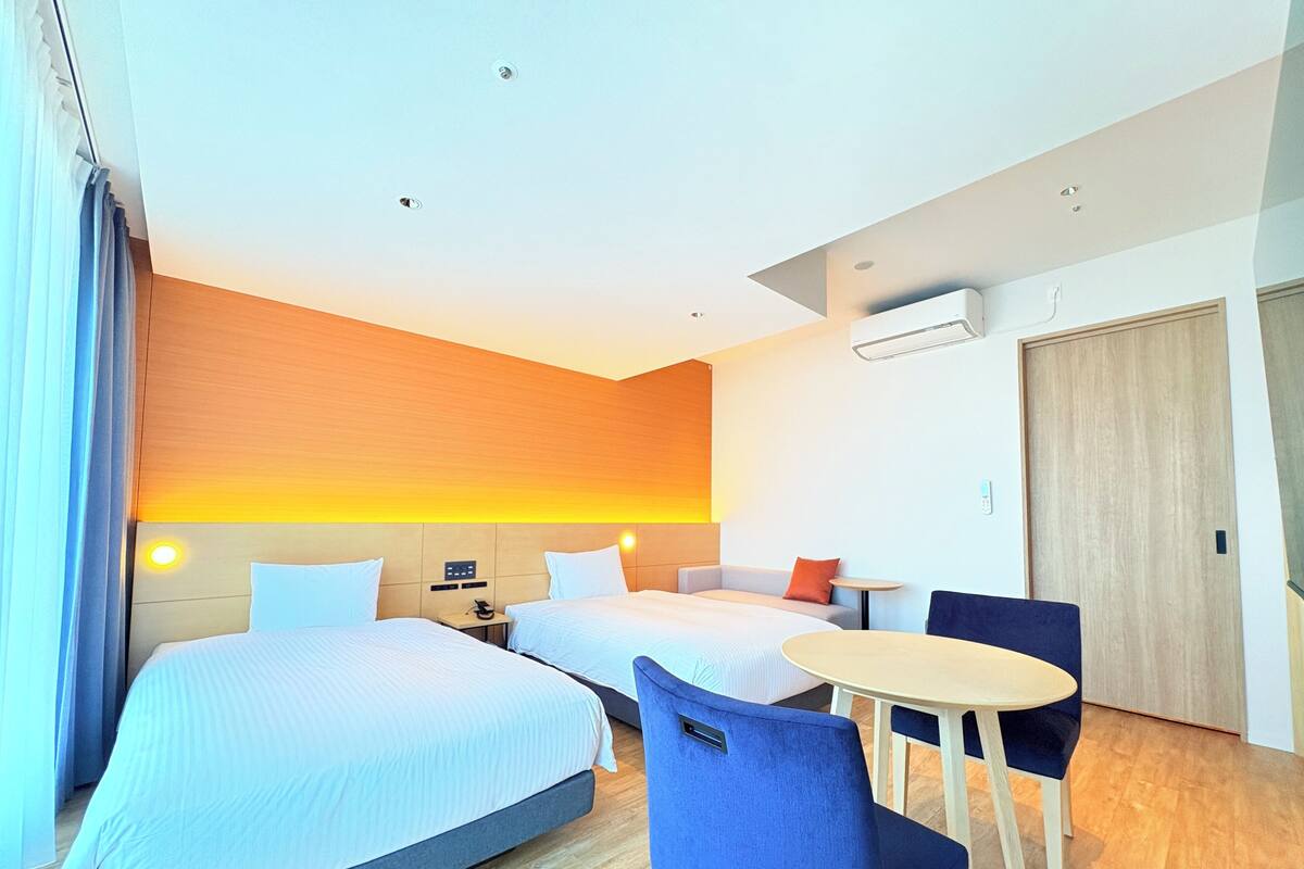Habitación de hotel con dos camas, una mesita, una silla y un sofá.