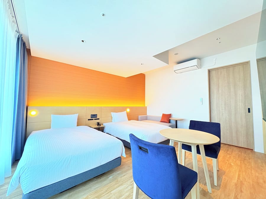 Ein Hotelzimmer mit zwei Betten, einem kleinen Tisch, einem Stuhl und einem Sofa.