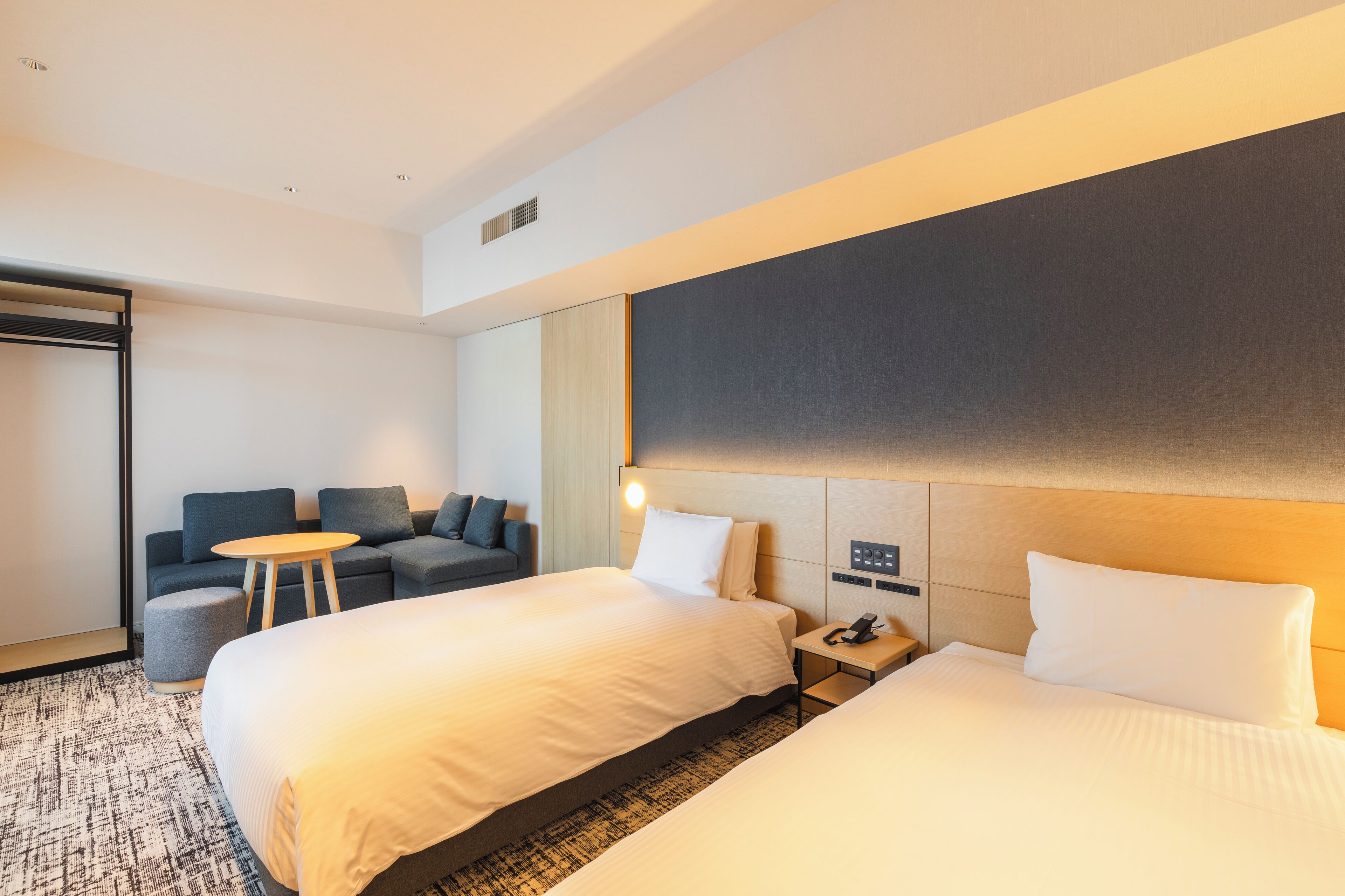 Habitación de hotel con dos camas, un sofá, una mesita redonda y una mesita de noche con un teléfono.