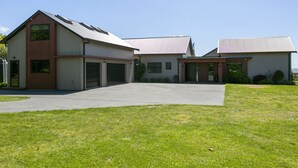 A two-story building with a garage, a covered driveway, and a grassy lawn. - Lake Taupō Hideaway Apartment in Acacia Bay (Lake Taupō)