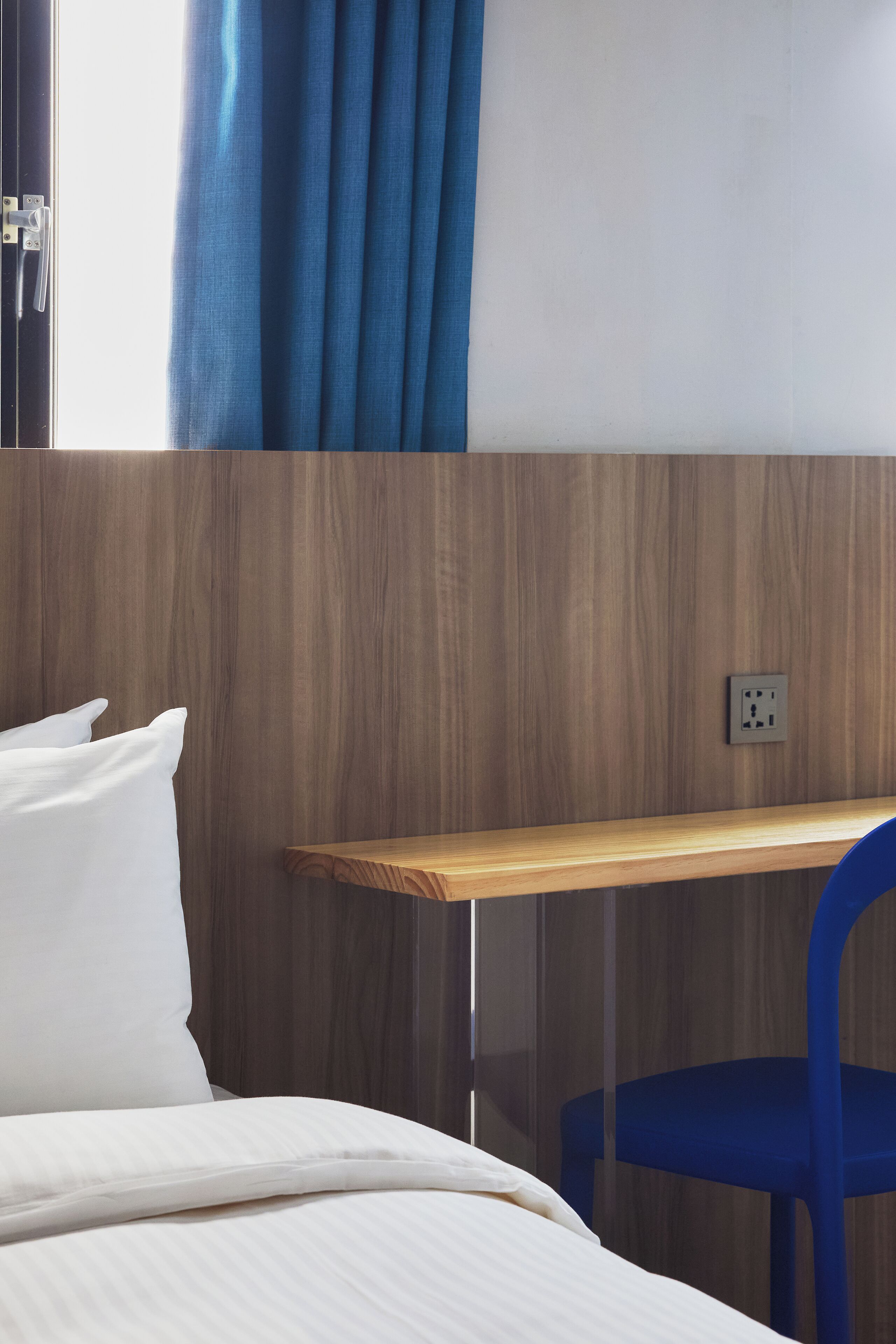 Ein Hotelzimmer mit einem Bett, einem Holztisch, einem blauen Stuhl und einer wandmontierten Steckdose.