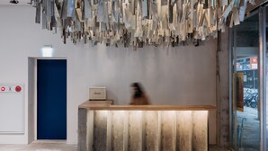 A reception desk with a wooden finish and a modern, abstract art installation above it. - The Blue By Just Inn (Taipei)