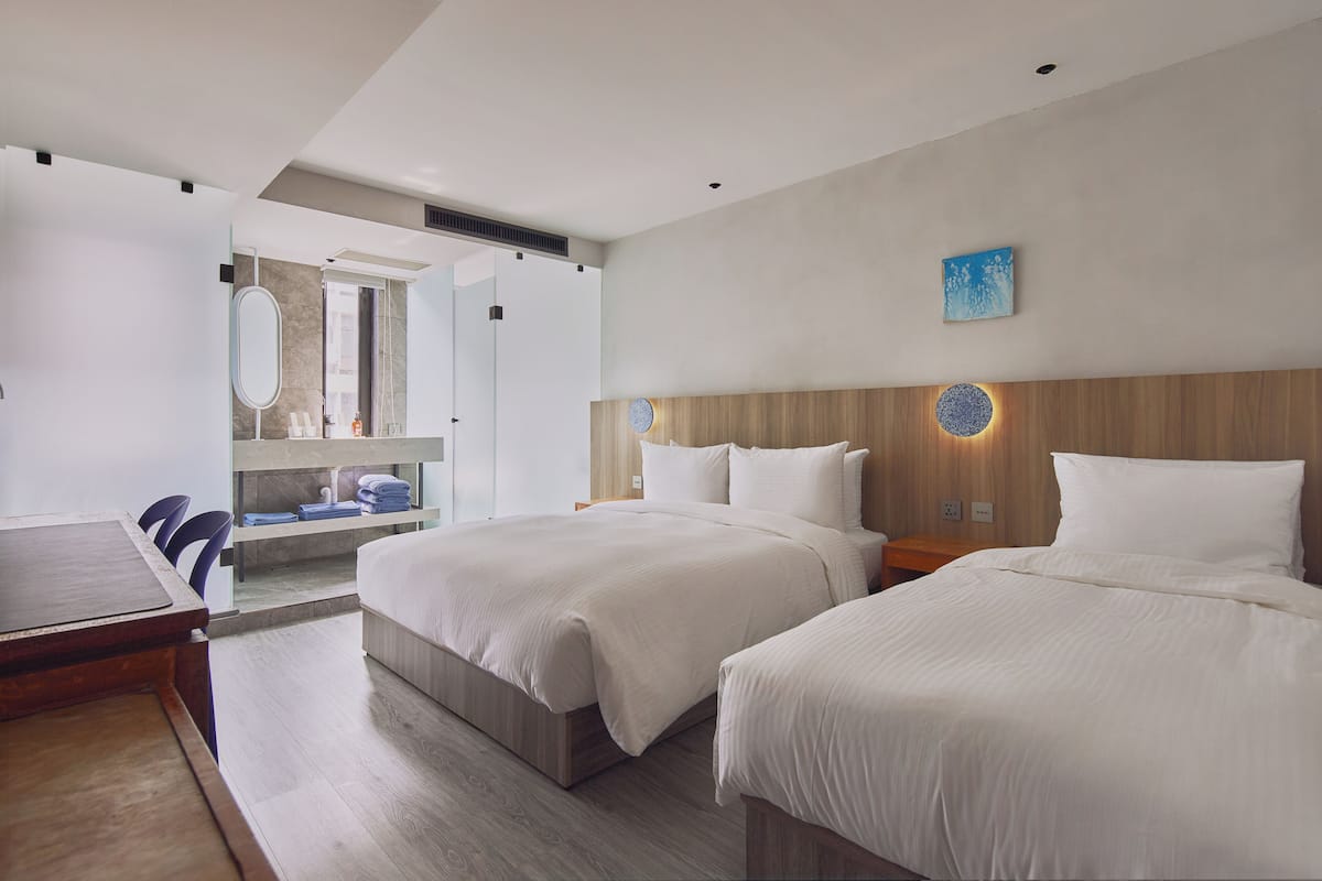 A modern hotel room with two beds, a wooden headboard, a large mirror, and a small table.