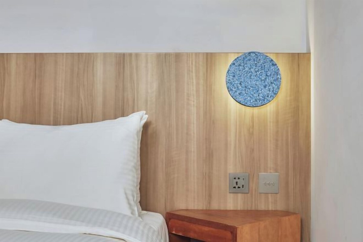 A bedroom with a wooden headboard, a bedside table, and a wall-mounted light fixture.