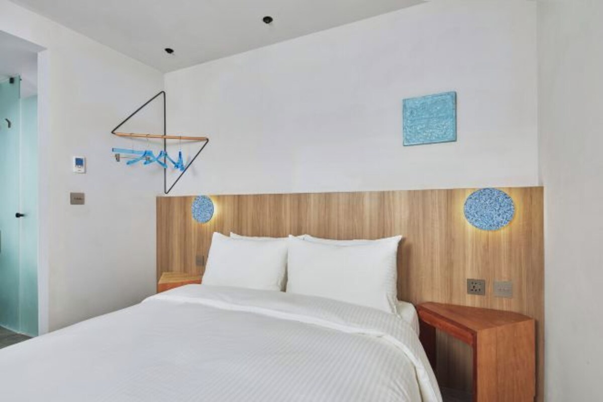 Une chambre d’hôtel moderne avec un grand lit, une tête de lit en bois et deux appliques murales rondes.