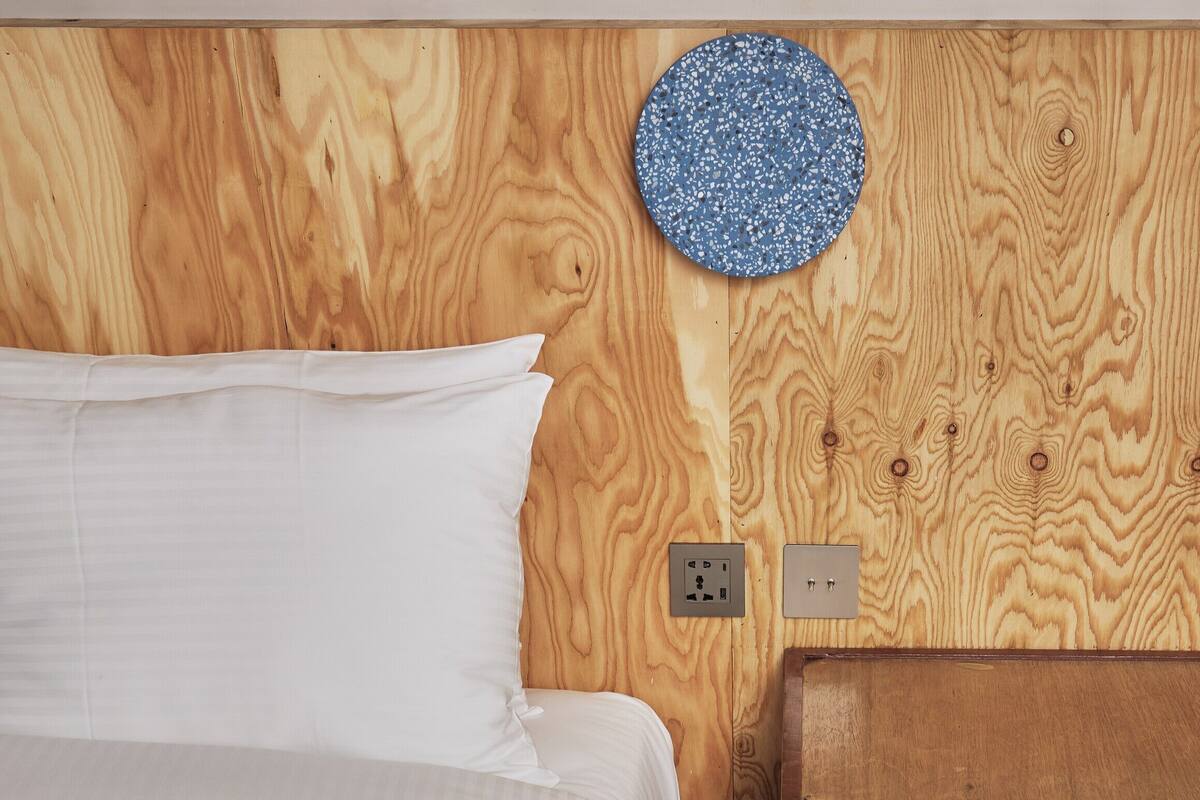 A bed with white linens, a wooden headboard, and a blue textured wall hanging.