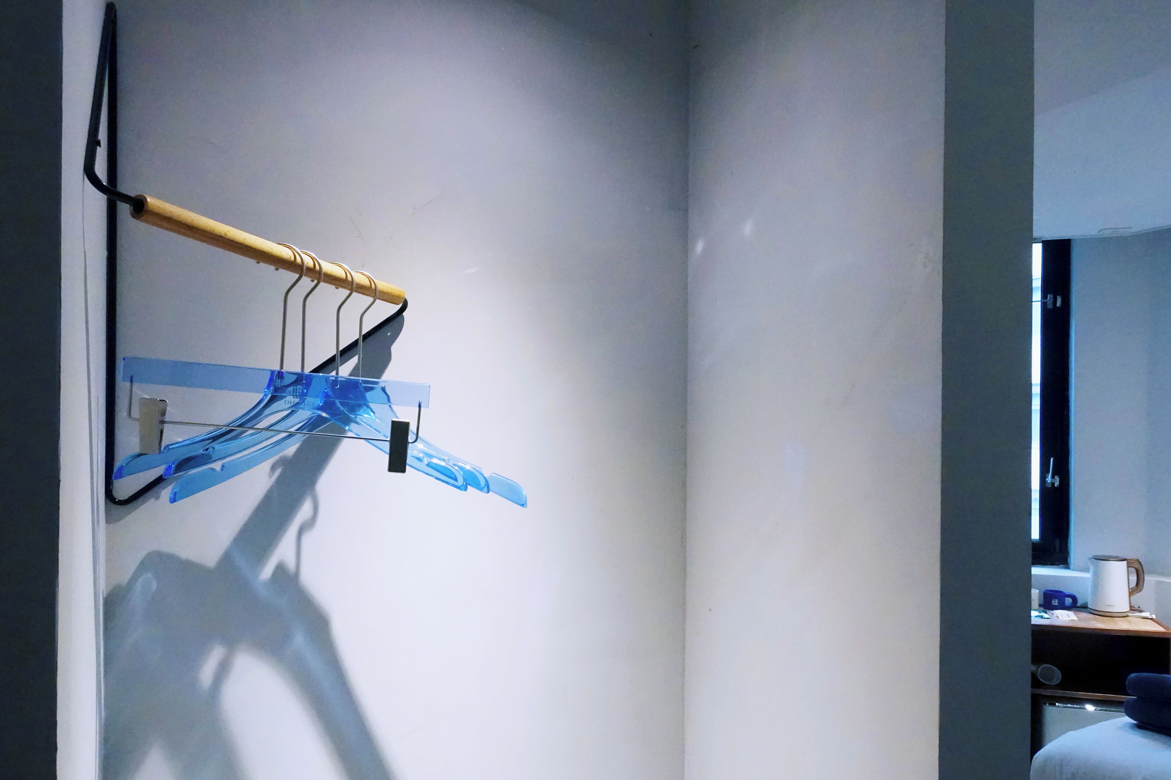 A room with a wooden rack holding blue clothespins, a window with a view, and a small table with a kettle.