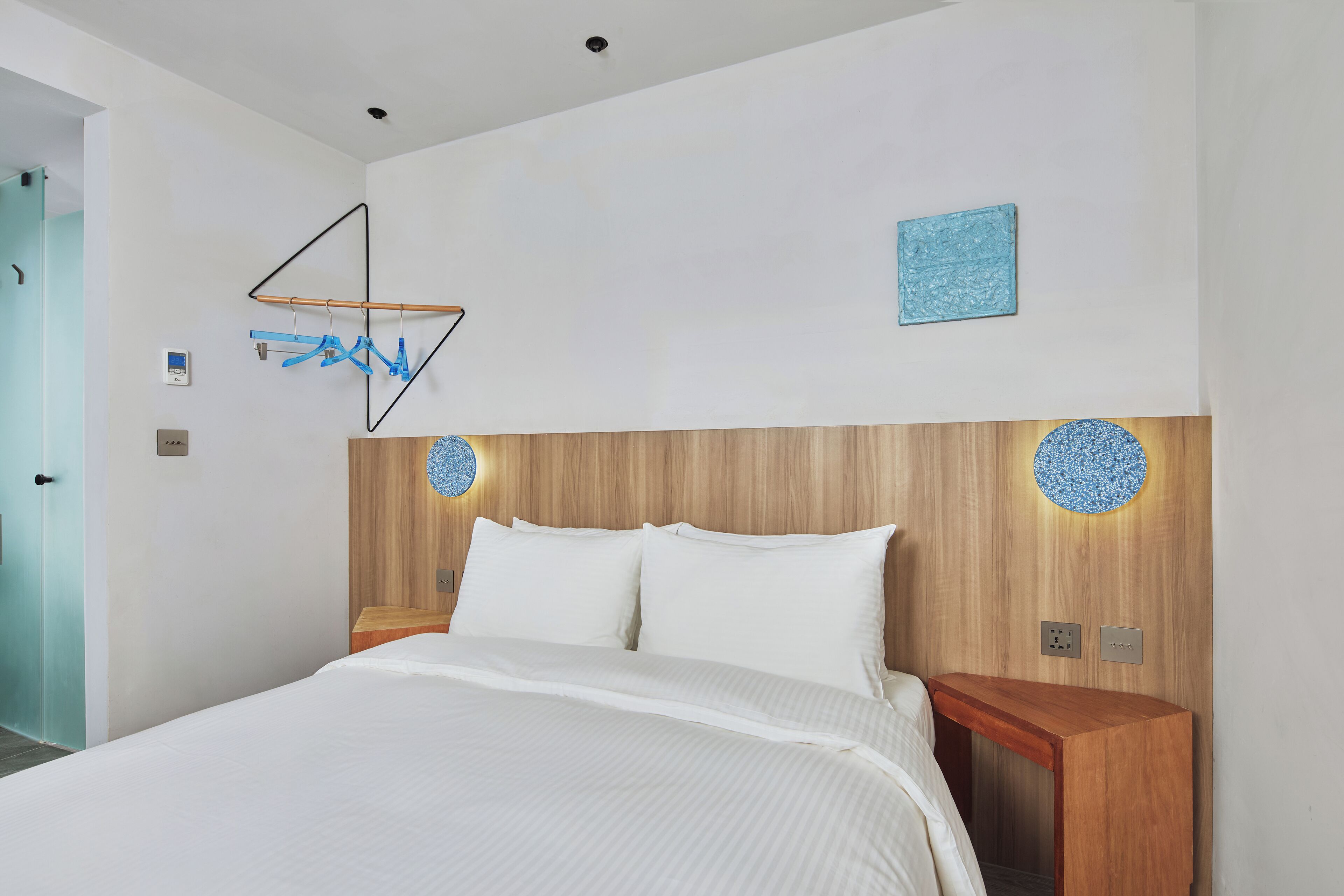 A modern bedroom with a wooden headboard, a bed with white linens, a wooden nightstand, and a wall-mounted light fixture.