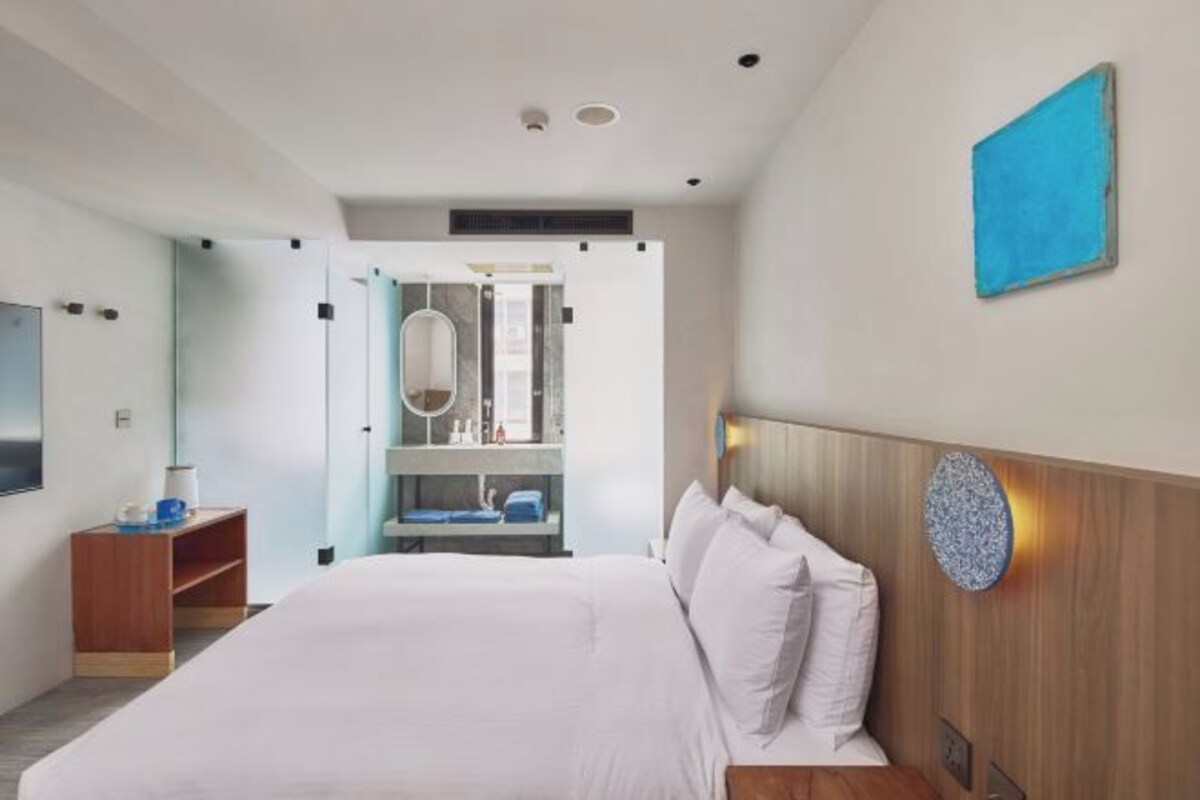 Une chambre d’hôtel moderne avec un grand lit, une tête de lit en bois, une armoire intégrée et une petite table de chevet en bois.