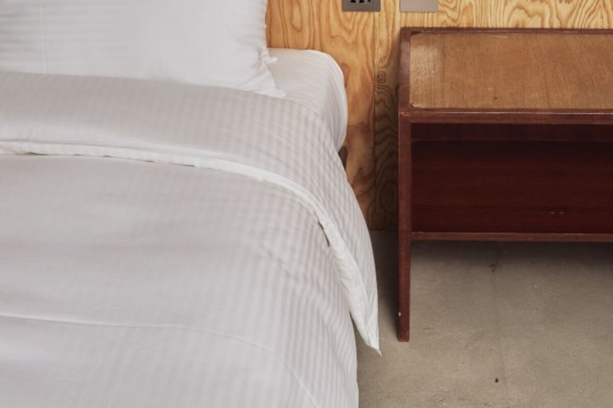 Un lit avec une literie blanche, une tête de lit en bois et une table de chevet en bois dotée d’un tiroir.