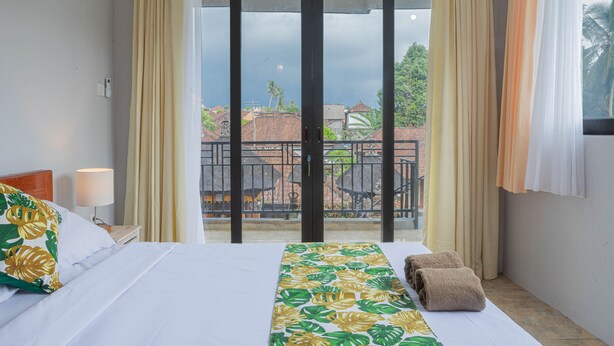 A hotel room with a bed, a nightstand, a lamp, a window with curtains, and a view of the outside. - Nobody Inn Laplapan (Ubud)