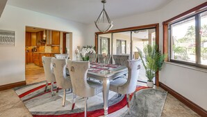 Een eetruimte met een glazen tafel, grijs gestoffeerde stoelen, een rood-grijs gestreept tapijt en een kroonluchter.