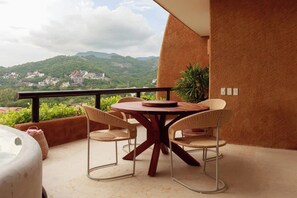 Un balcone con tavolo e sedie, vista su un paesaggio montuoso e un edificio in lontananza.