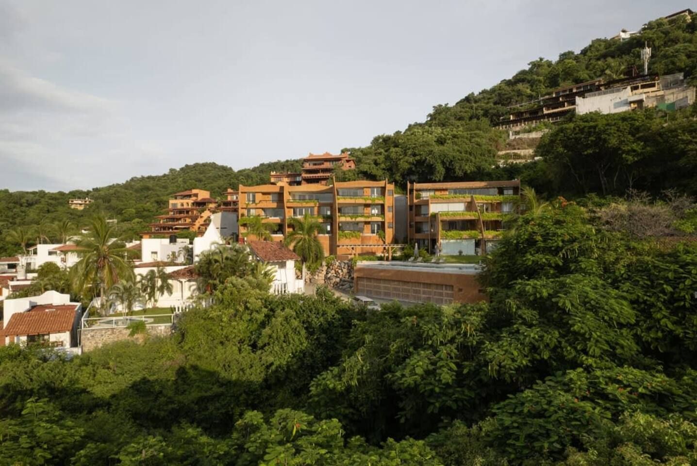 Una zona residencial en una ladera con edificios modernos de varios pisos, abundante vegetación y un cielo despejado.