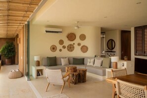 A modern living room with a sectional sofa, a dining table, and a coffee table. There are woven wall decorations and a ceiling fan.