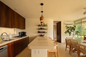 A modern kitchen with a central island, wooden cabinets, and a hanging pendant light. - Luxury Penthouse | Private Pool Steps from La Ropa (Zihuatanejo)