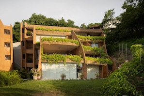 Un edificio de varios pisos con un diseño arquitectónico singular, con balcones con plantas y un techo inclinado.