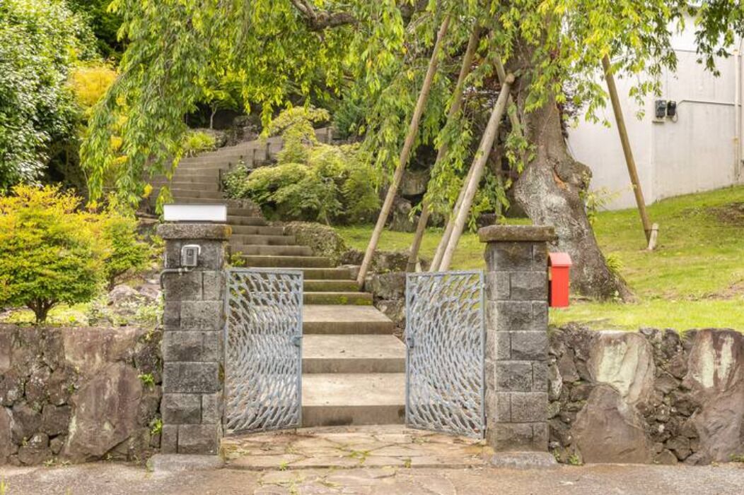 A stone staircase leading up to a gated entrance, surrounded by lush greenery and trees.