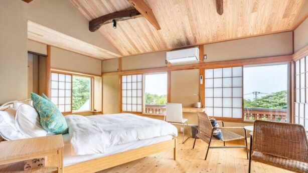 A traditional Japanese-style room with tatami flooring, a low wooden bed, and sliding shoji doors. - Spaciouse Private Hot Spring, Spotless 3 BDR with Stylish Modern Japanese Deco (Ito)