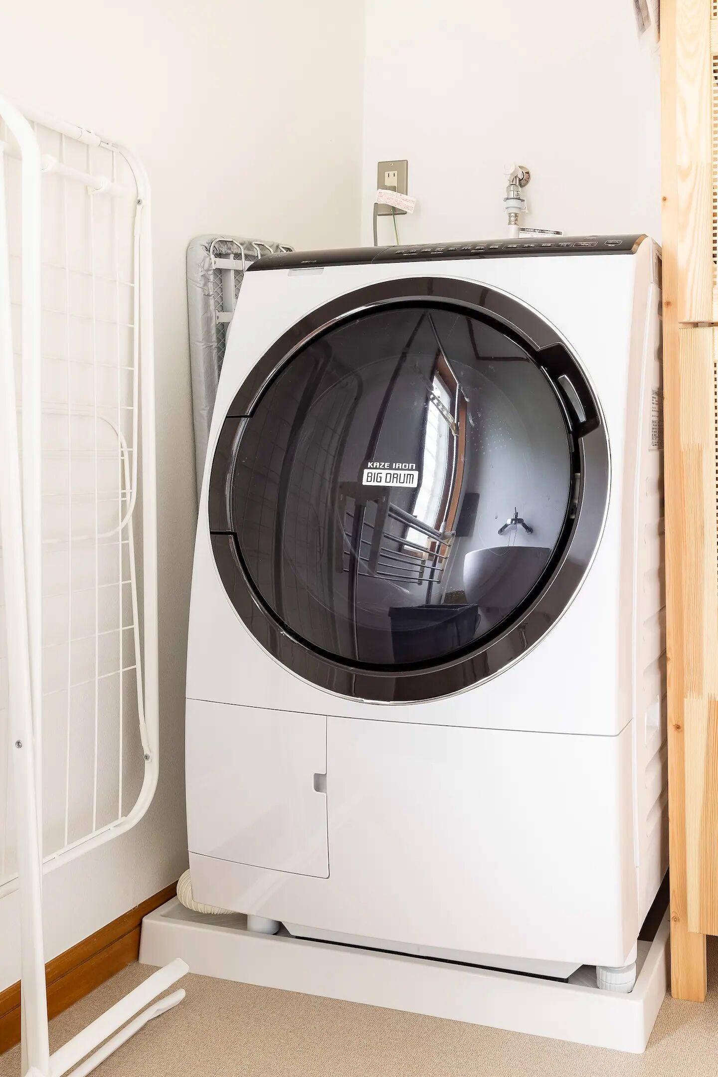 A front-loading white washing machine with a control panel on top, placed next to a white radiator and a wooden cabinet.