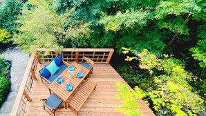 A wooden deck with a table and chairs, surrounded by lush greenery. - Spaciouse Private Hot Spring, Spotless 3 BDR with Stylish Modern Japanese Deco (Ito)