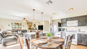 Una cocina moderna con refrigerador, microondas y estufa. Hay una mesa de comedor con sillas y una planta encima.