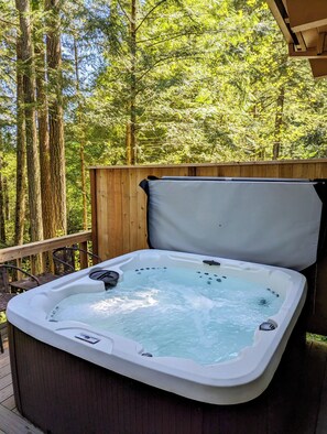 A hot tub on a wooden deck surrounded by tall trees.