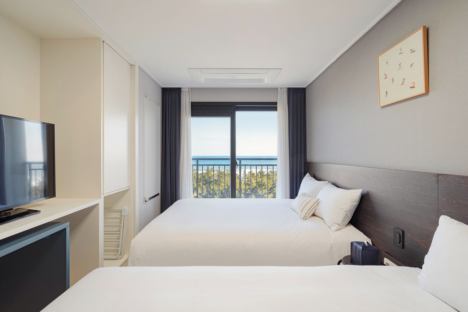 Ein Hotelzimmer mit zwei Betten, einem Fernseher und einem Balkon mit Meerblick.