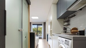A modern kitchen with a washing machine, a sink, and a window with a view of trees.