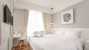 Habitación de hotel con una cama grande, un escritorio, una silla, una mesita de noche, un teléfono y un televisor montado en la pared.