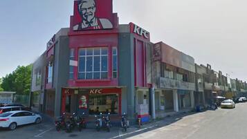 En KFC restaurant med et stort rødt og hvidt skilt, flere motorcykler foran og en række butikker langs gaden.