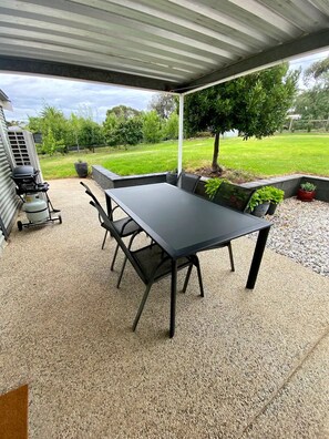 An outdoor patio with a table and chairs, a grill, and a covered area with a view of a grassy yard. - The Cottage at Seppeltsfield, Barossa Valley (Seppeltsfield)