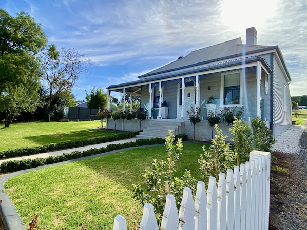 A two-story house with a covered porch, a well-maintained lawn, and a white picket fence. - The Cottage at Seppeltsfield, Barossa Valley (Seppeltsfield)