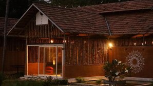 A rustic wooden building with a sloped roof, a large glass door entrance, and a decorative wall pattern. - Pura Vida Varkala (Varkala)