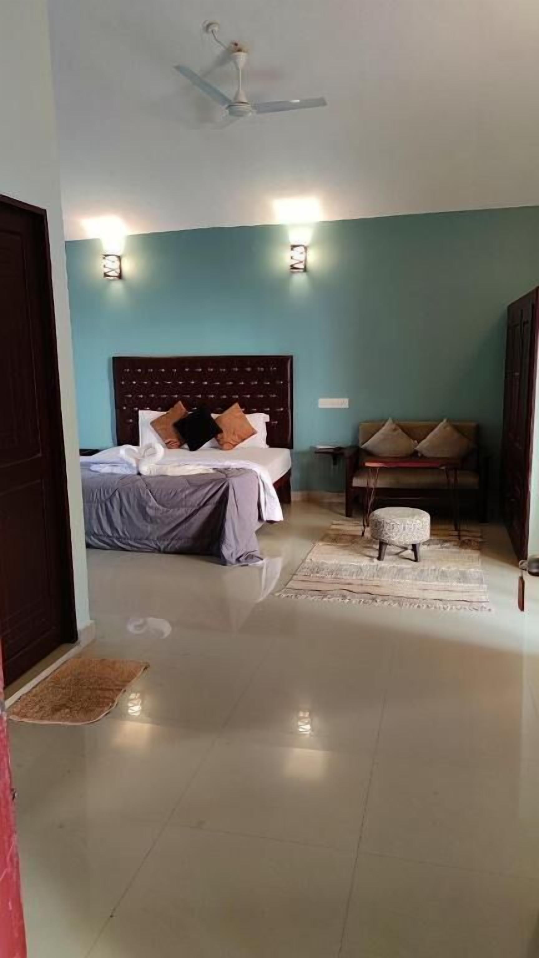 A bedroom with a bed, a sofa, a chair, a small table, and a ceiling fan.