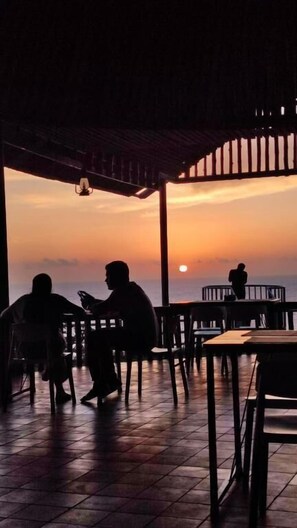A restaurant with outdoor seating overlooking the ocean at sunset. - Pura Vida Varkala (Varkala)