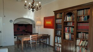 Un coin repas avec une table et des chaises en bois, un lustre et une grande bibliothèque remplie de livres.