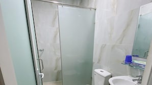 Pieni kylpyhuone, jossa on wc, pesuallas ja lasinen suihkuseinä.