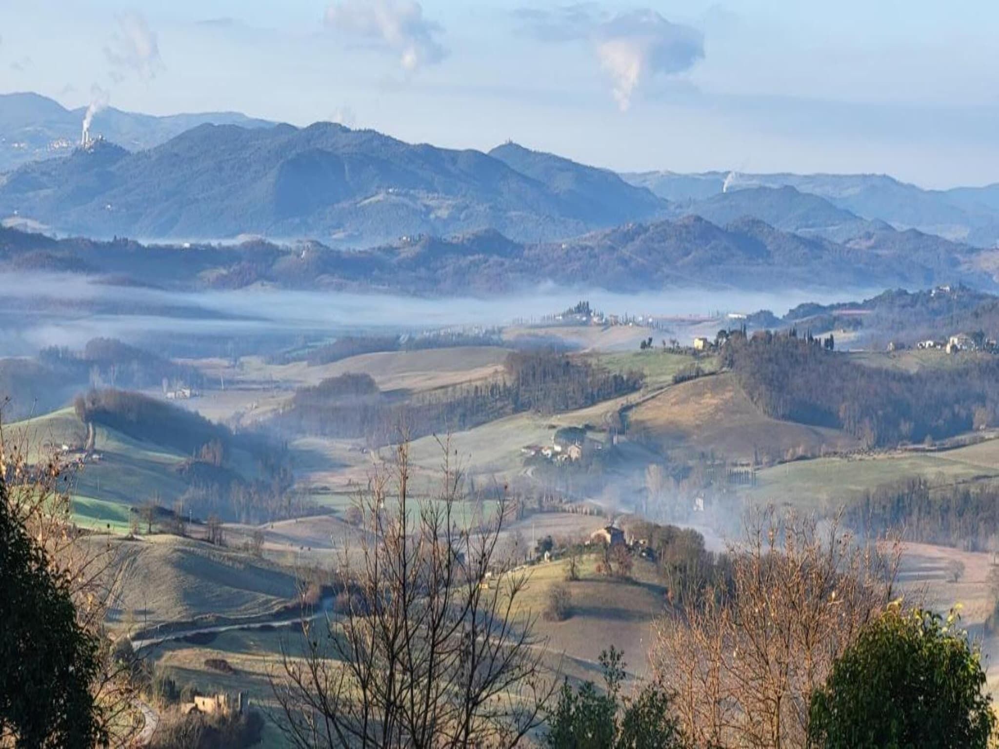 Une vue panoramique d’un paysage montagneux, avec des collines ondoyantes, des arbres dispersés et quelques bâtiments.