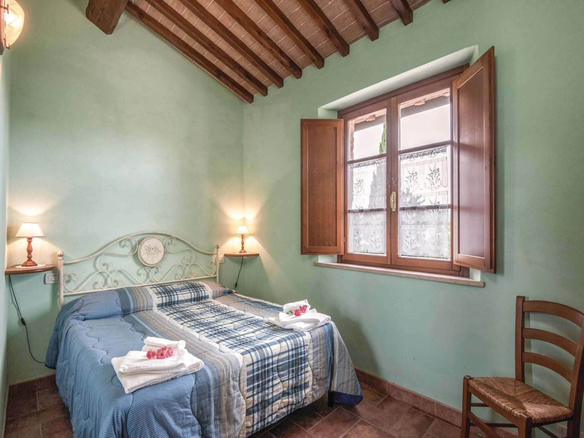 Une chambre à coucher avec un lit, deux lampes de chevet, une fenêtre avec des volets en bois et une chaise.