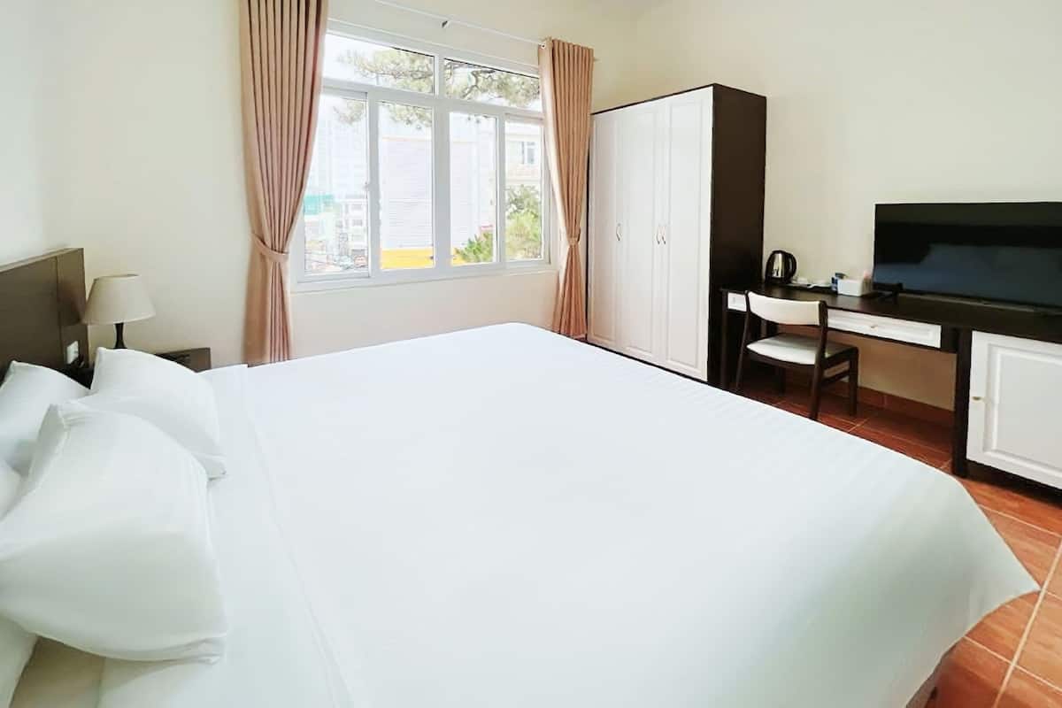 A hotel room with a large bed, a desk with a chair, a television, and a wardrobe.