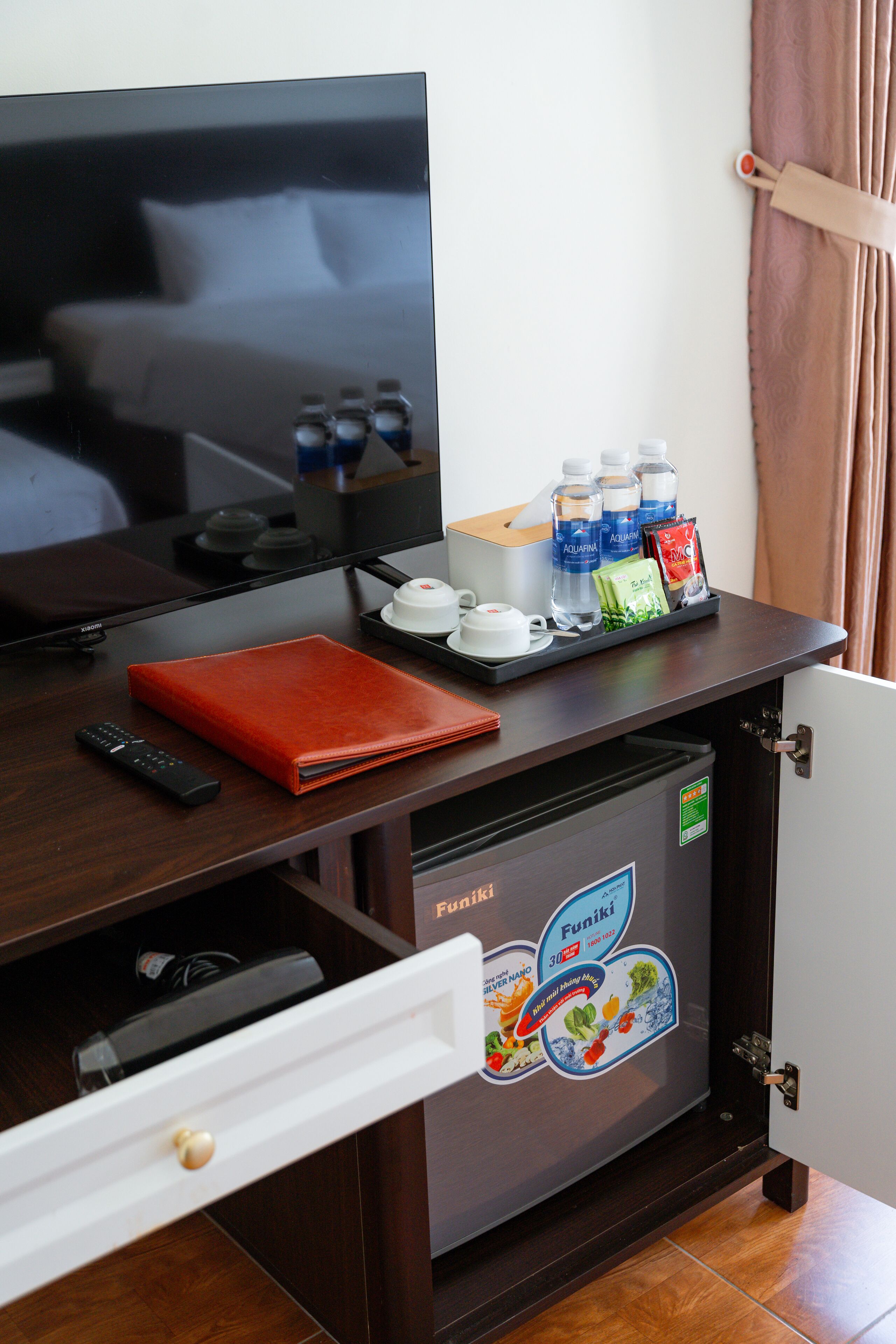 Hotelkamer met een televisie, een minibar, een afstandsbediening, een rode map en een minibar deur met een Funiki sticker.