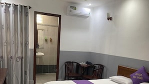 A hotel room with a bed, a desk, a chair, a bathroom visible through an open door, and an air conditioning unit on the wall. - Dai Hong Hotel - by Bay Luxury (Ho Chi Minh City)
