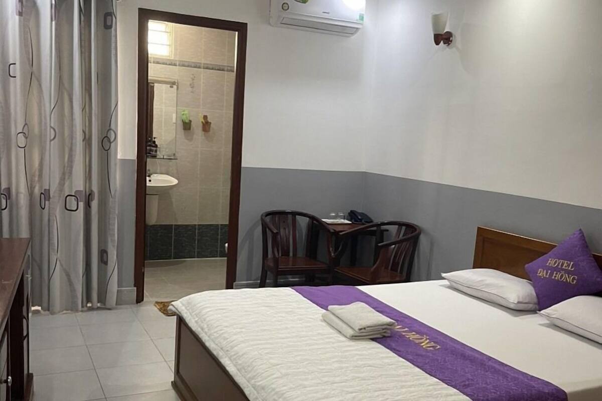 Ein Hotelzimmer mit Bett, Schreibtisch, Stuhl und offenem Badezimmer. Eine Klimaanlage ist an der Wand angebracht.