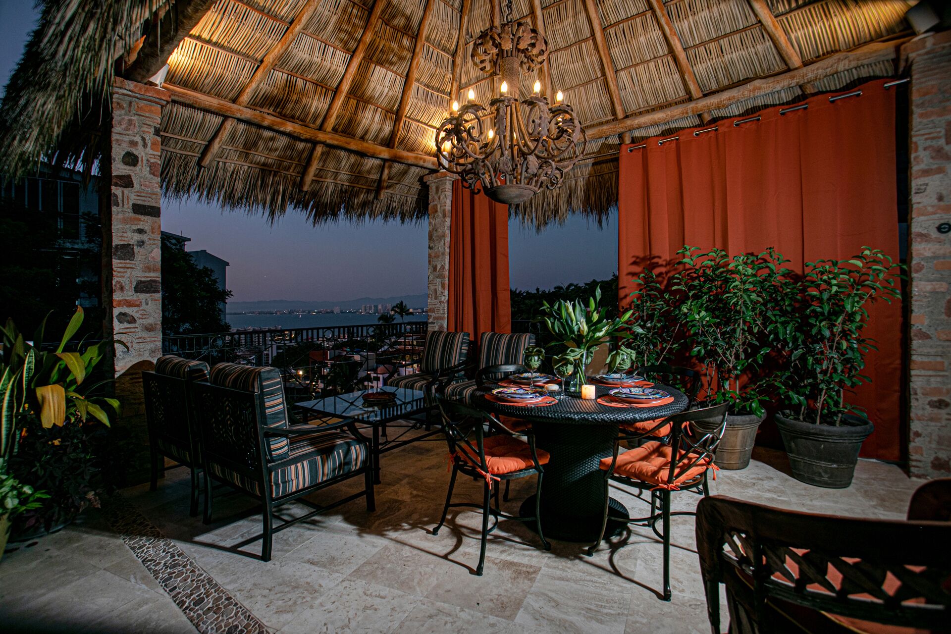 An outdoor dining area with a thatched roof, wicker furniture, and potted plants.