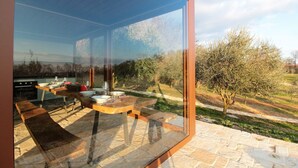 Ein moderner Essbereich im Freien mit Glasveranda, Steinboden und Blick auf die umliegende Landschaft.