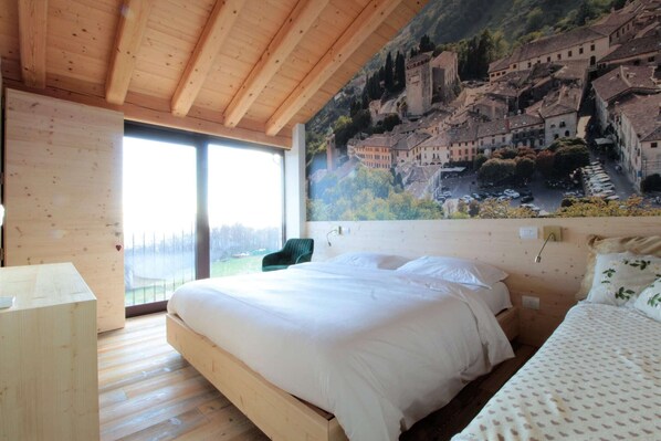 Une chambre avec un plafond en bois, un grand lit avec une literie blanche, un fauteuil vert et une fresque représentant une ville historique sur le mur.